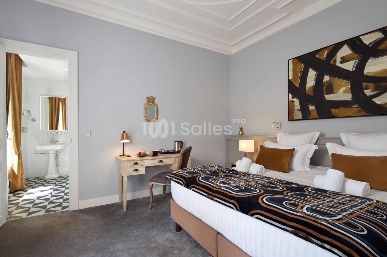 Chambre lumineuse avec lit double, bureau, salle de bain attenante et décoration moderne aux tons neutres et chaleureux.