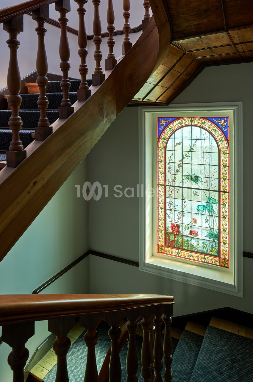 Escalier en bois avec une fenêtre en vitrail coloré représentant des motifs floraux et végétaux.