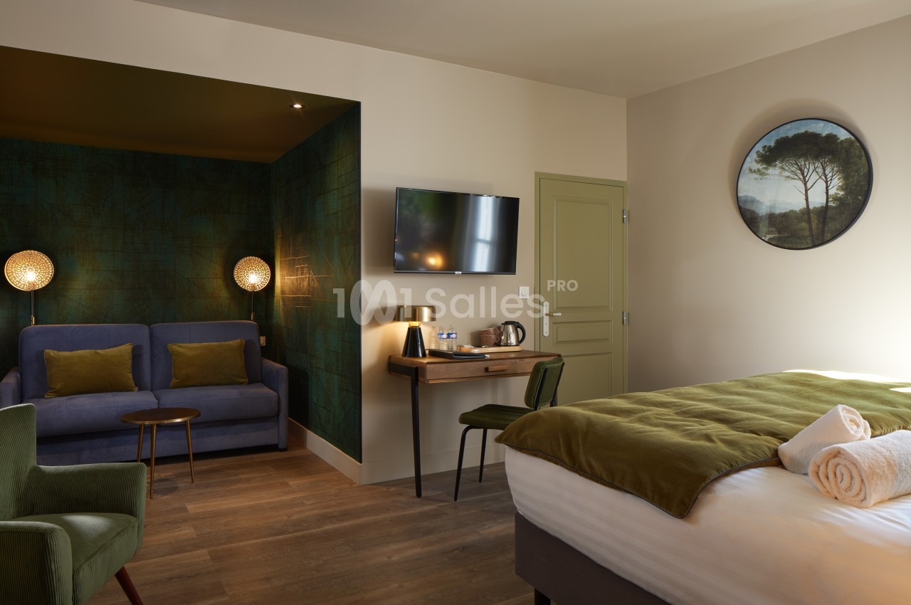 Chambre d'hôtel avec lit double, canapé, bureau, télévision murale et éclairage tamisé dans une ambiance chaleureuse.