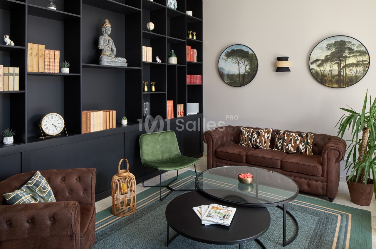 Salon moderne avec canapé en cuir, étagères noires remplies de livres et décorations, table basse ronde et plantes.