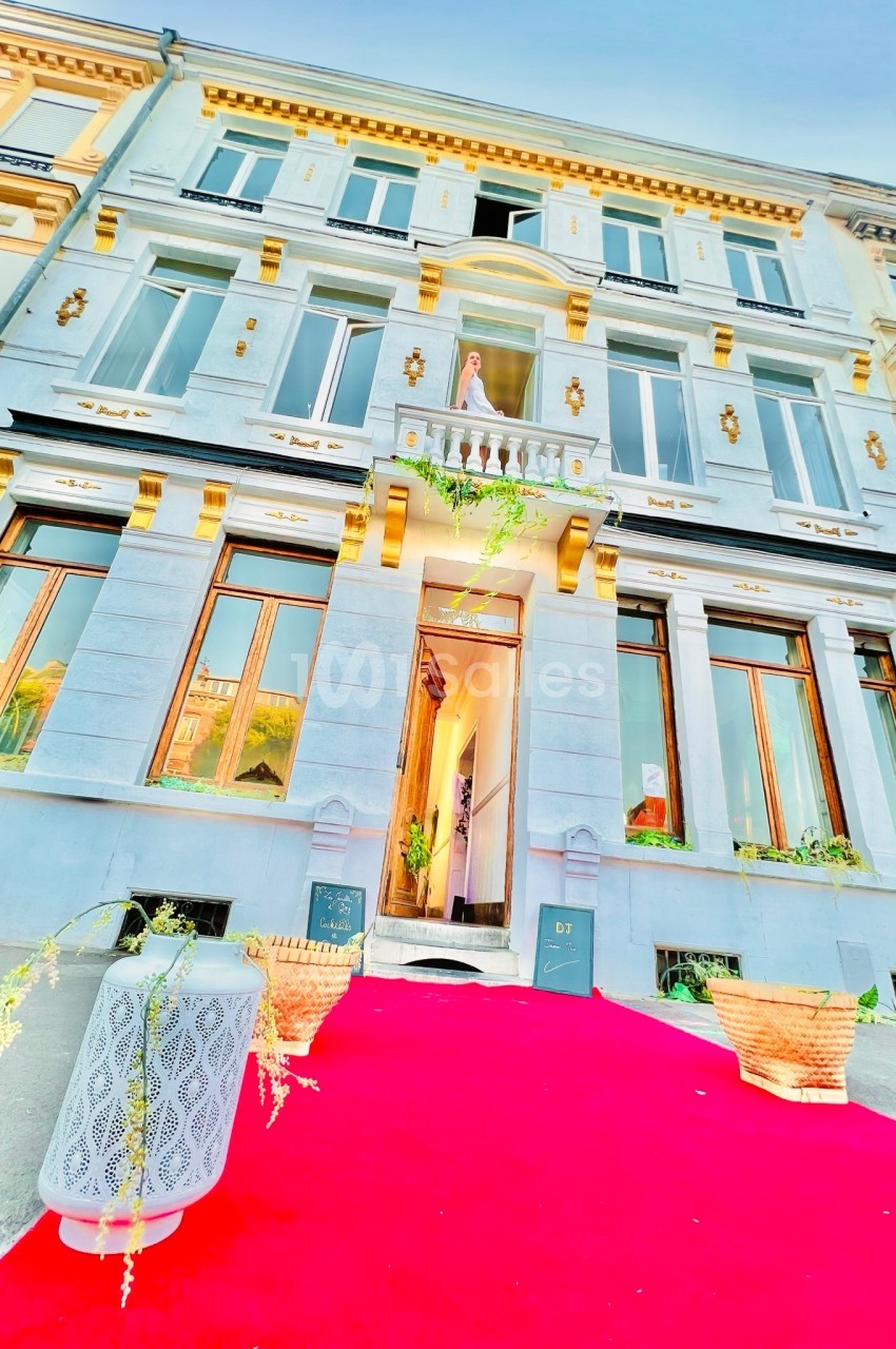 Façade d'un bâtiment élégant avec balcon, tapis rouge à l'entrée et décorations végétales.