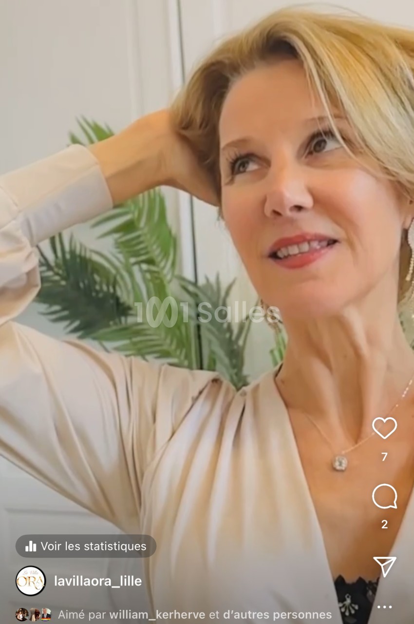 Femme souriante, regardant vers le haut, posant les mains derrière la tête, avec une plante en arrière-plan.