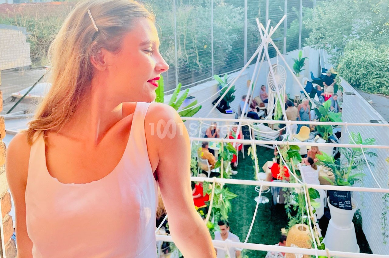 Une femme en robe blanche regarde au loin depuis un balcon, surplombant une fête en plein air avec des décorations et des…