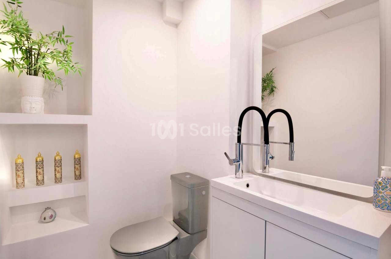 Salle de bain moderne avec lavabo double, miroir, toilettes grises et étagères décorées de plantes et flacons.
