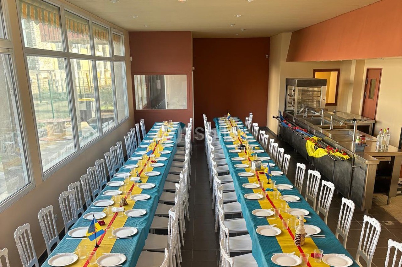Salle de réception avec deux longues tables dressées, nappes colorées et chaises blanches alignées.