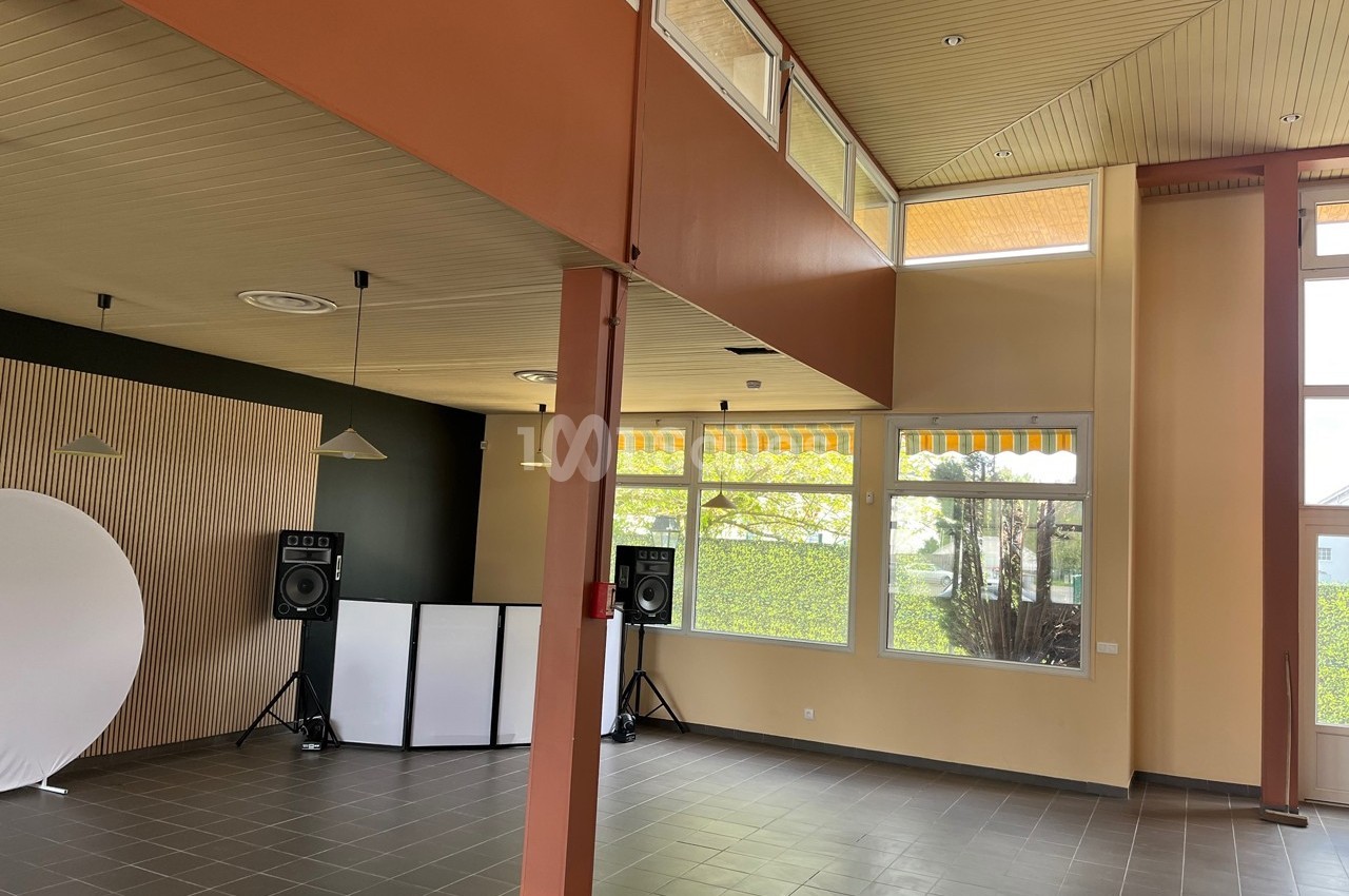 Salle lumineuse avec grandes fenêtres, murs clairs, sol en carrelage gris, équipements audio et fond blanc installés.