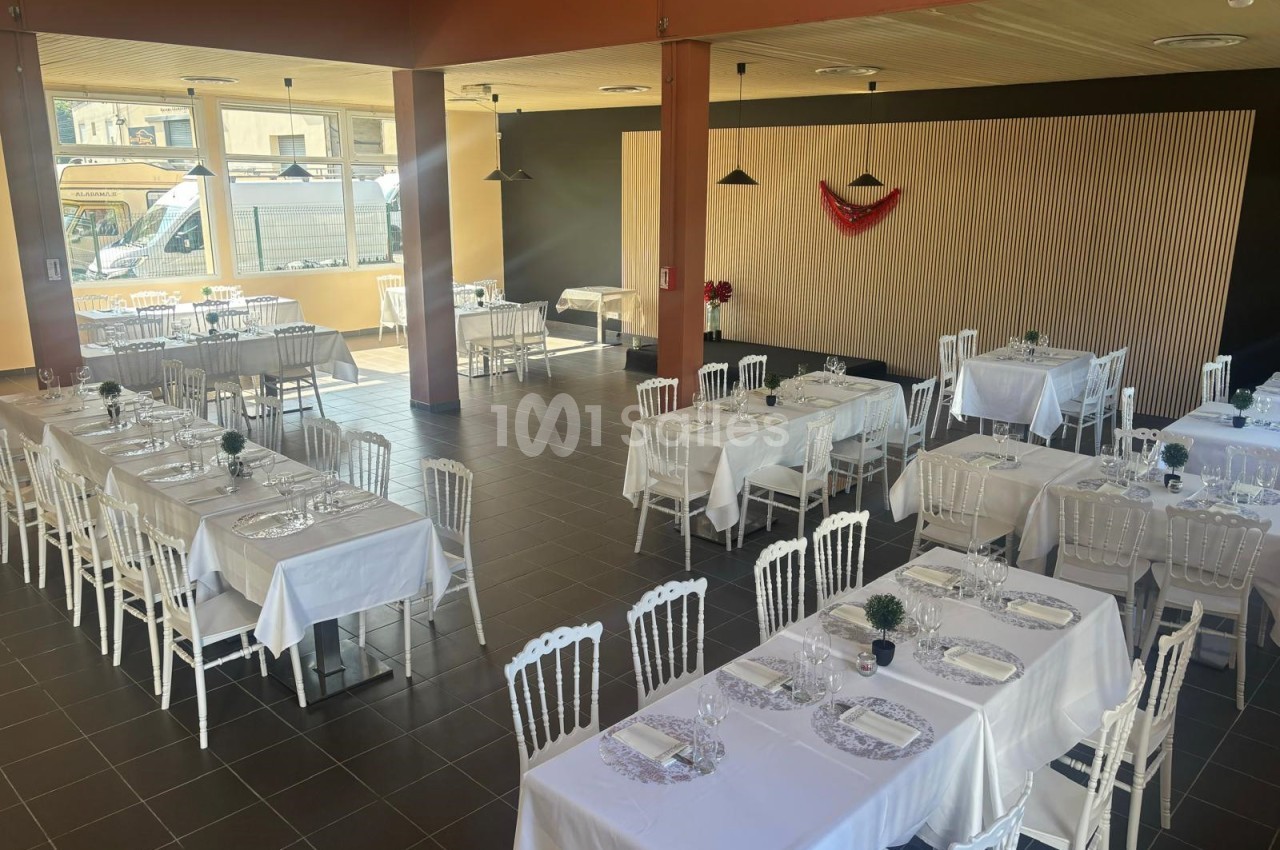 Salle de réception lumineuse avec tables dressées, nappes blanches et chaises blanches, décor minimaliste.