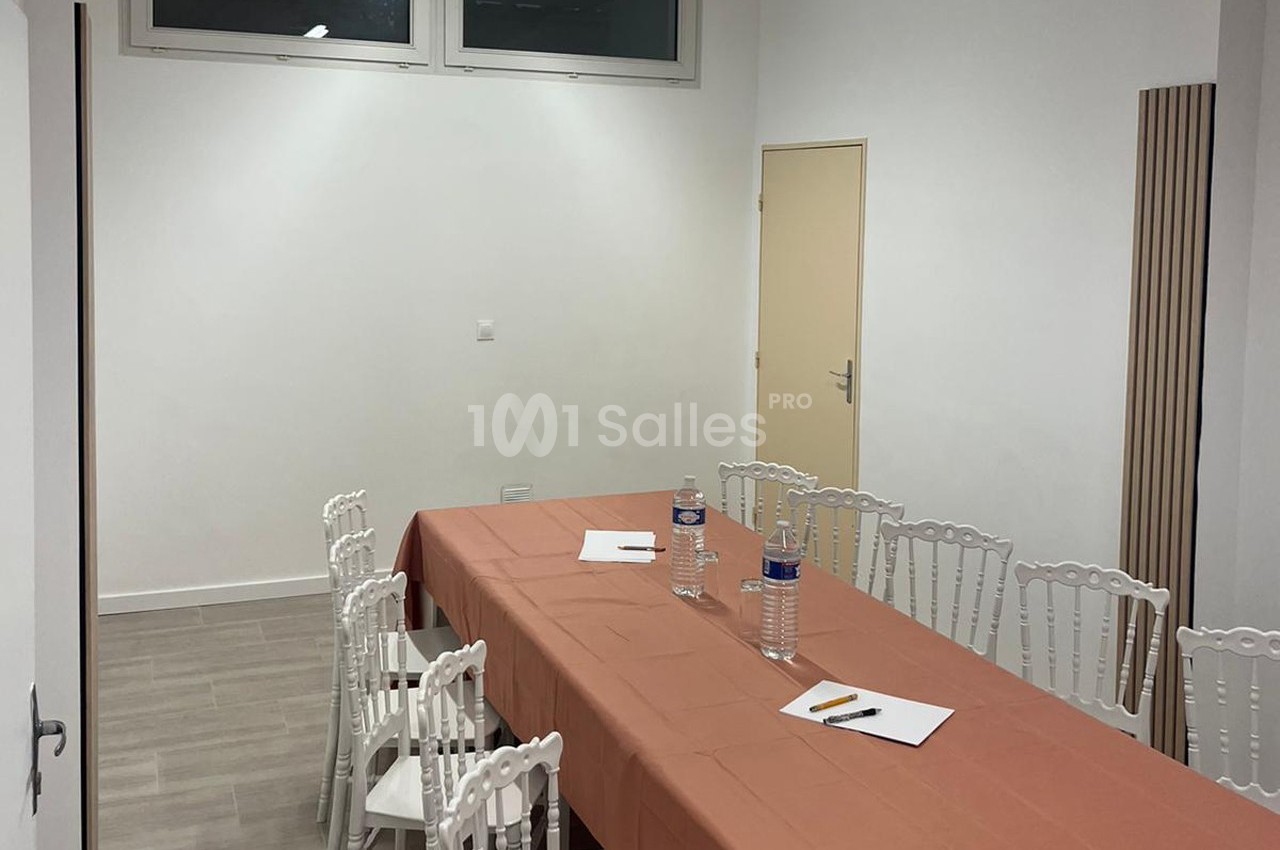 Salle de réunion avec une table rectangulaire couverte d'une nappe orange, entourée de chaises blanches.