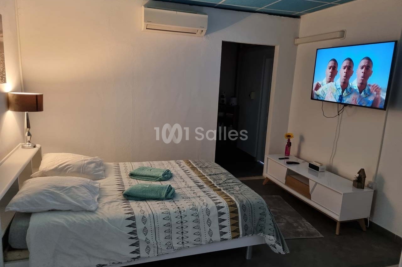 Chambre lumineuse avec lit double, linge plié, télévision murale allumée et mobilier moderne.