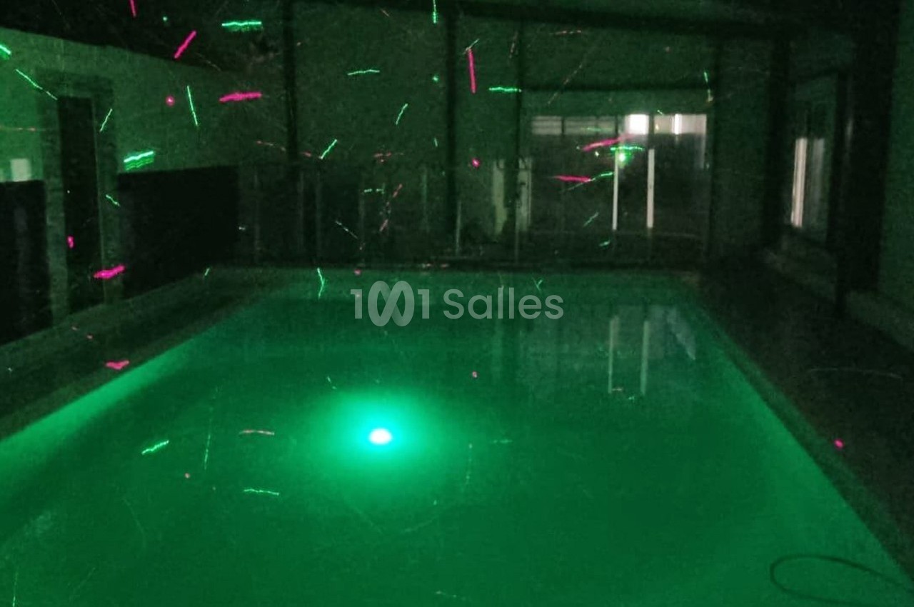 Piscine intérieure éclairée par des lumières vertes et roses dans une ambiance sombre.