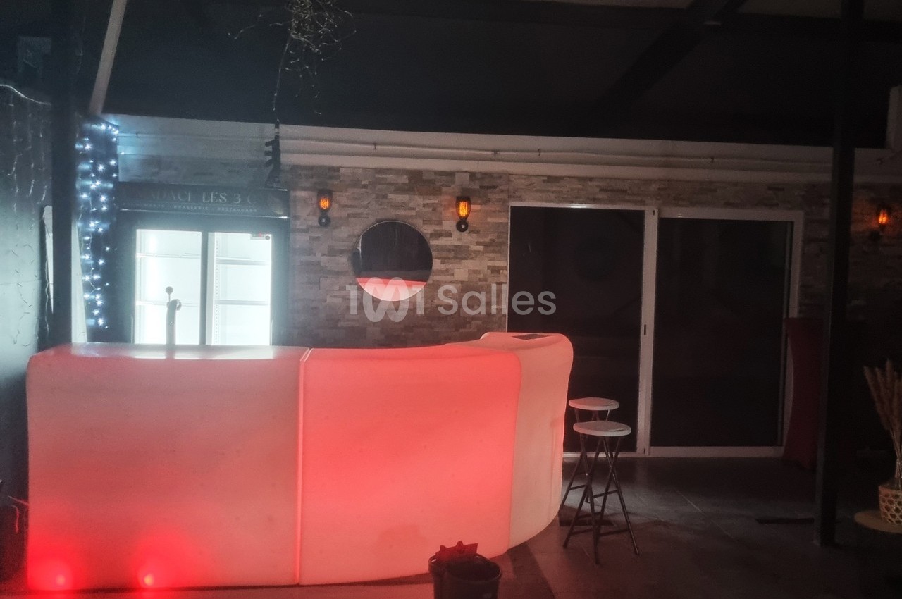 Comptoir lumineux rouge dans un espace intérieur sombre avec murs en pierre, tabourets et éclairages muraux.