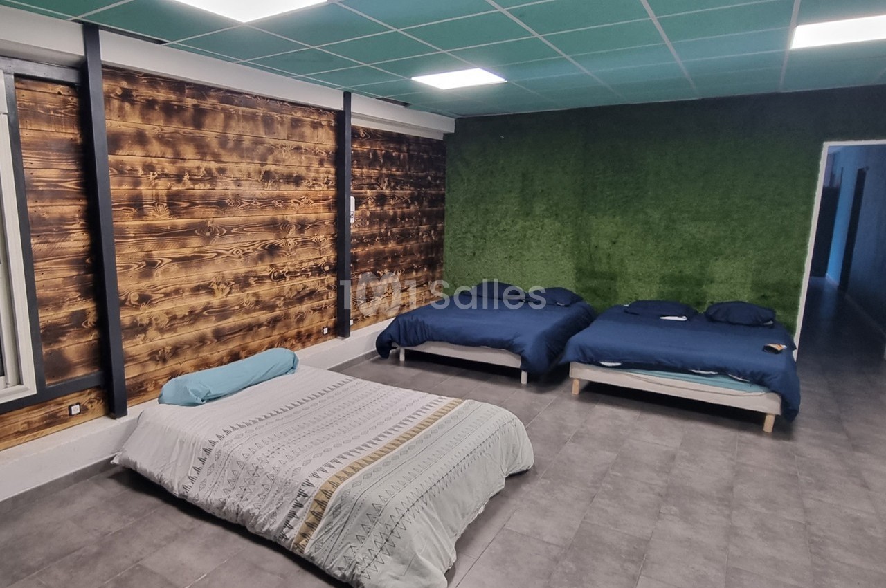 Trois lits dans une pièce avec mur en bois, mur vert texturé, plafond à dalles et sol en carrelage gris.