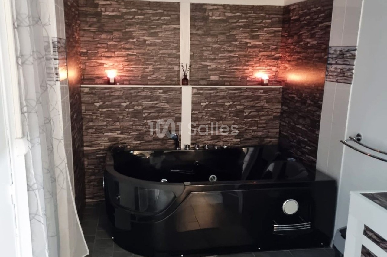 Baignoire noire moderne dans une salle de bain avec murs en fausses pierres et éclairage tamisé par deux bougies.
