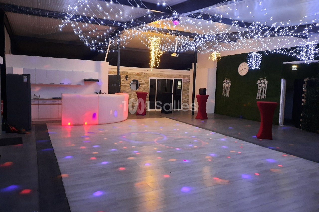Salle de réception décorée avec des guirlandes lumineuses, un comptoir blanc et une piste de danse éclairée.