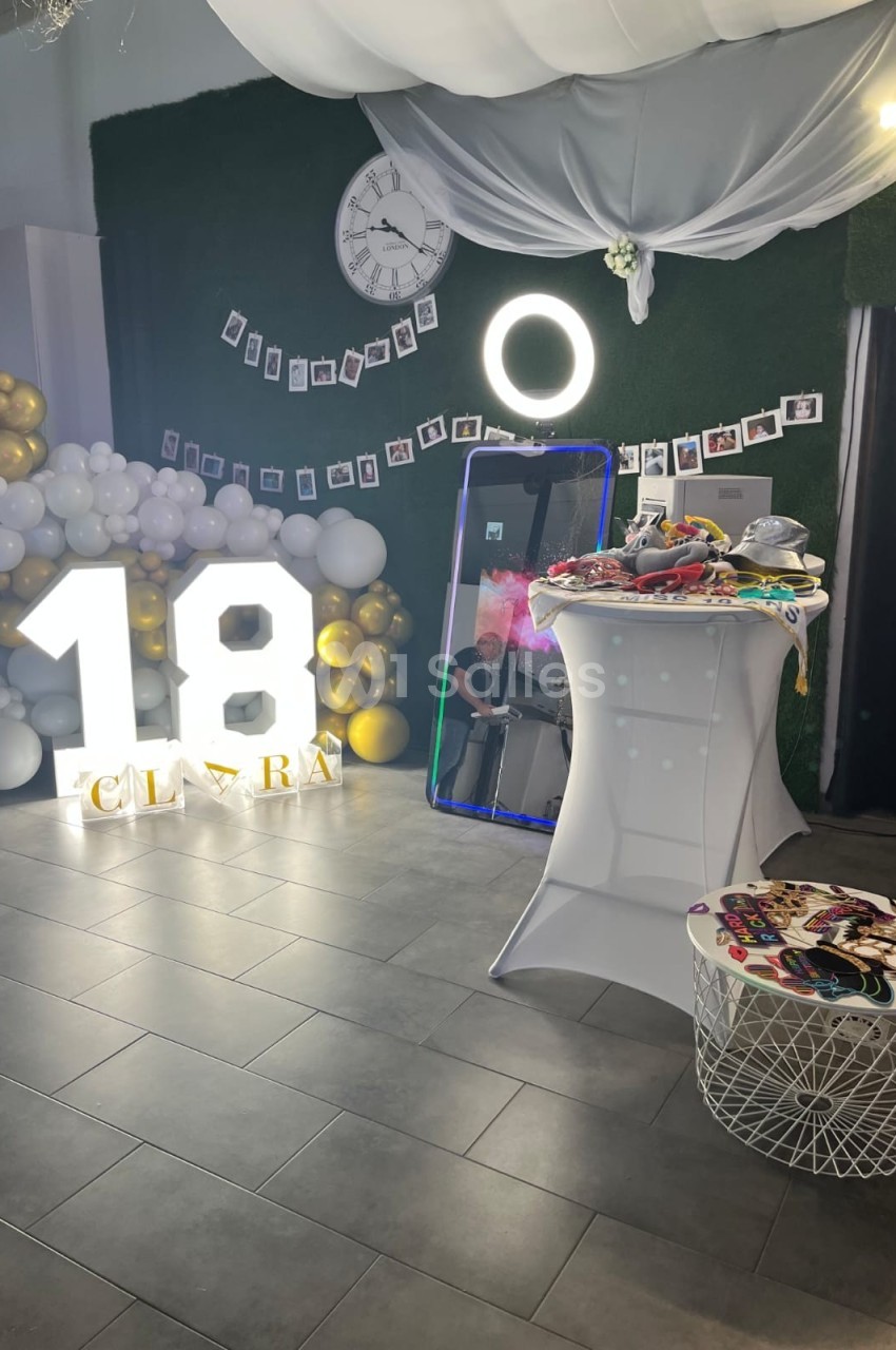 Décoration d'anniversaire avec ballons, chiffres lumineux ’18’, miroir interactif et accessoires sur une table.