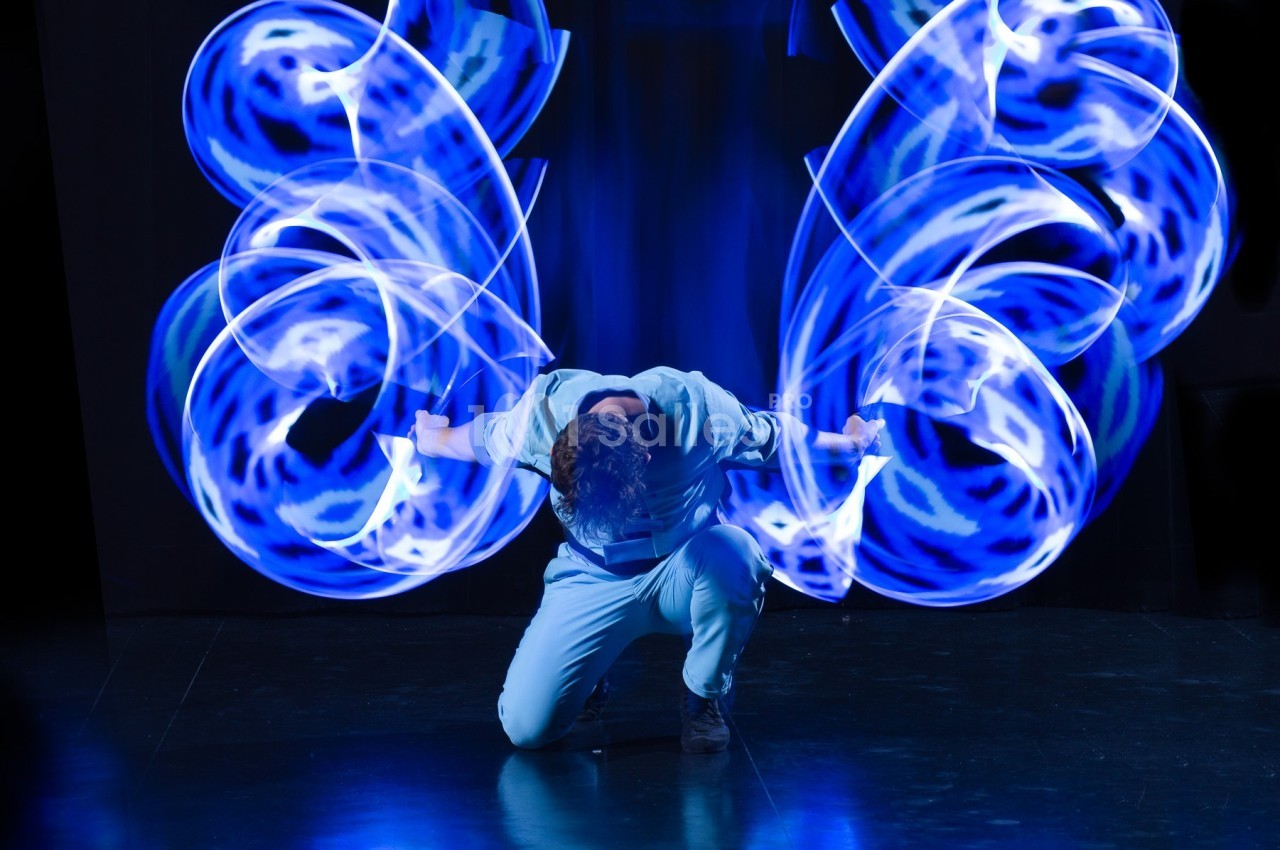 Personne agenouillée dans un décor sombre, entourée de motifs lumineux bleus en mouvement.
