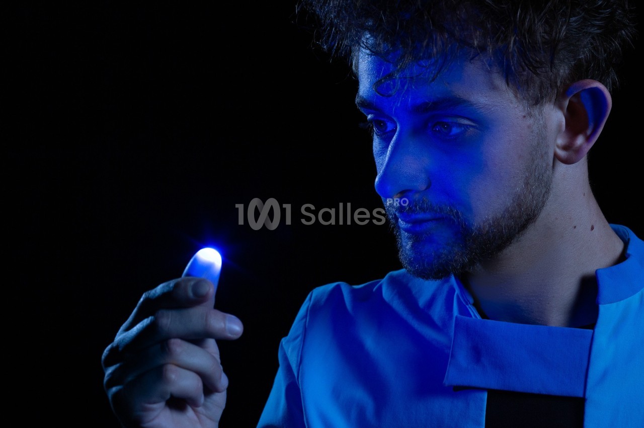 Un homme observe attentivement une lumière bleue brillante émanant de son doigt dans un environnement sombre.