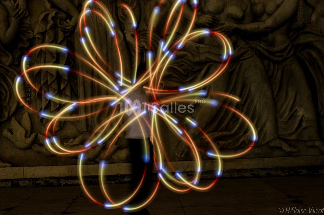 Personne manipulant des lumières colorées en mouvement créant des motifs lumineux devant une fresque sculptée.