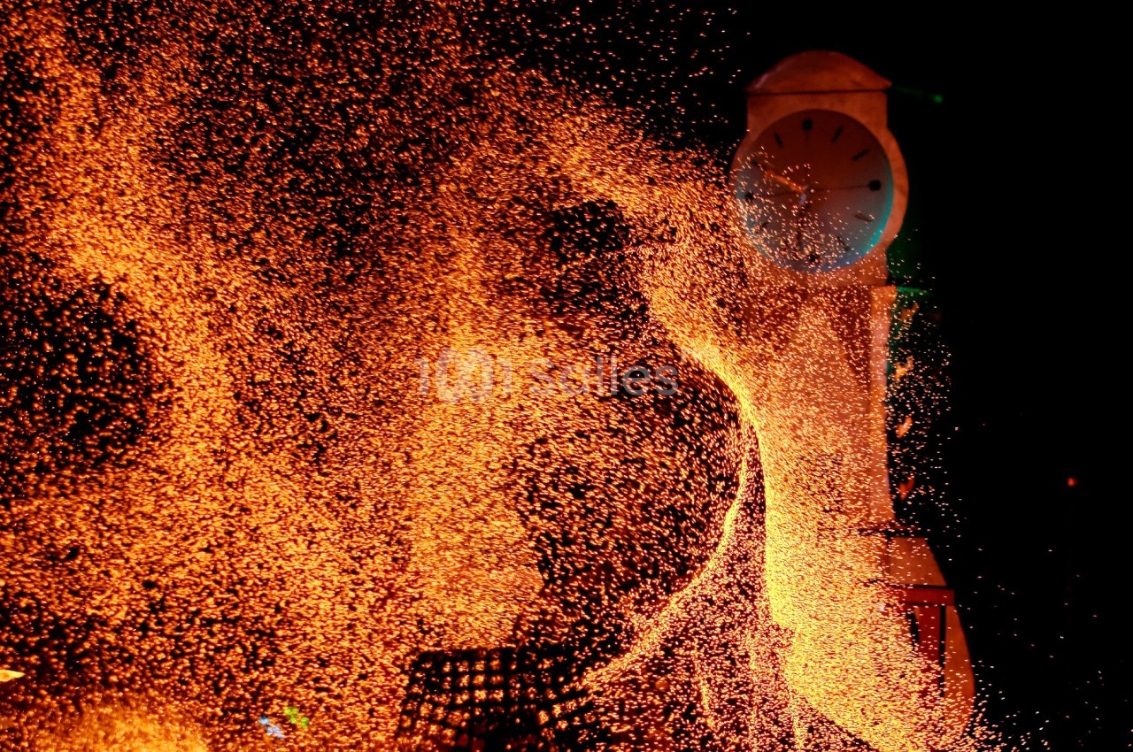 Projection d'étincelles orange devant une horloge illuminée dans l'obscurité.