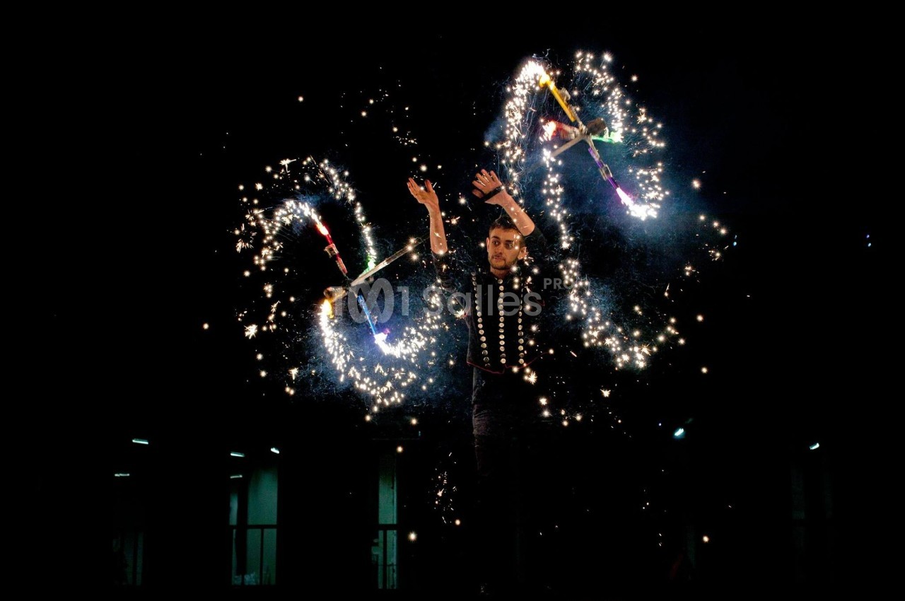 Un jongleur manipule des objets enflammés produisant des étincelles lumineuses dans l'obscurité.