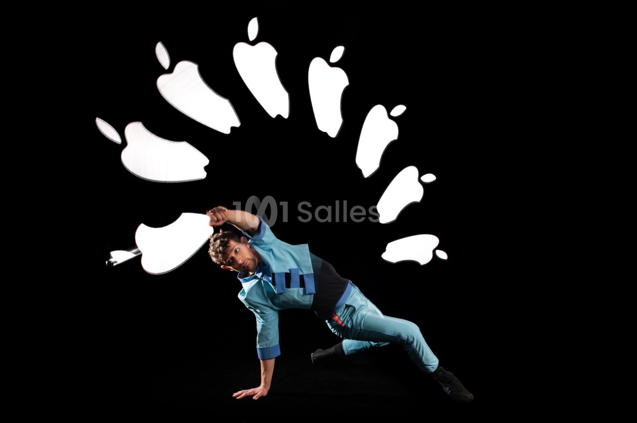Un danseur en tenue bleue effectue une figure au sol, entouré de formes lumineuses en arc sur fond noir.