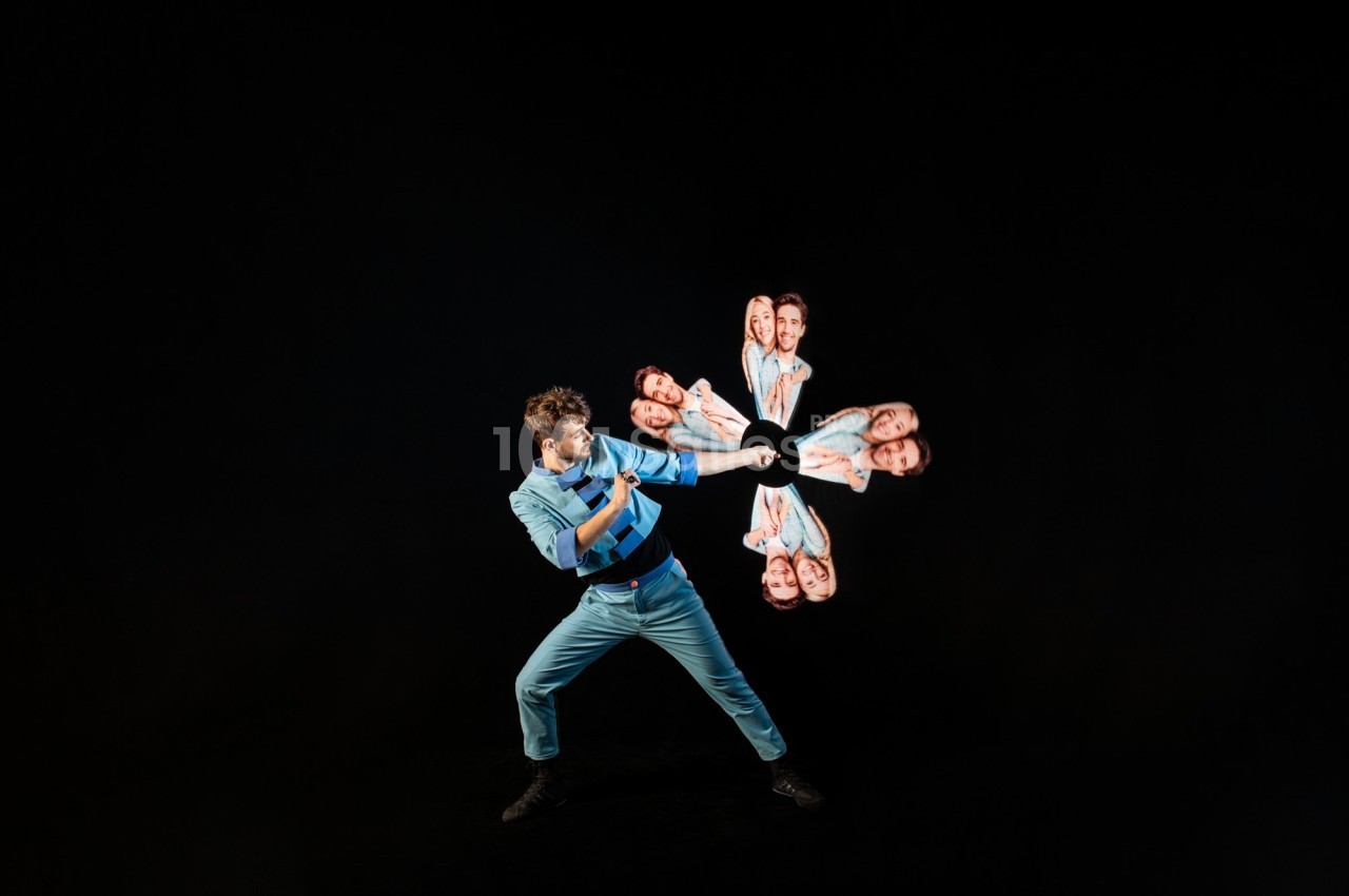 Un homme en tenue bleue effectue un mouvement dynamique avec des images de visages en rotation autour de sa main.
