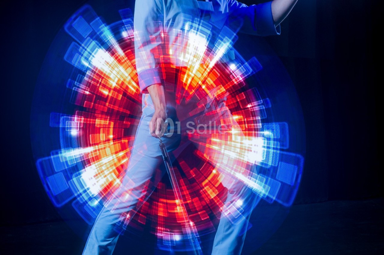 Une personne en tenue claire tient un objet devant un effet lumineux circulaire rouge et bleu en arrière-plan.