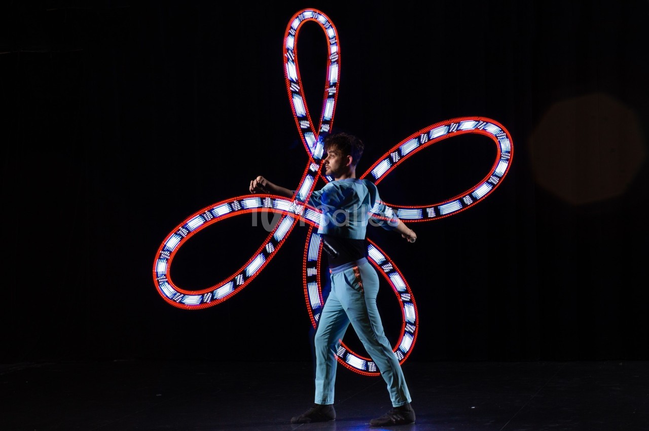 Un artiste jongle avec des anneaux lumineux formant des motifs colorés sur une scène sombre.
