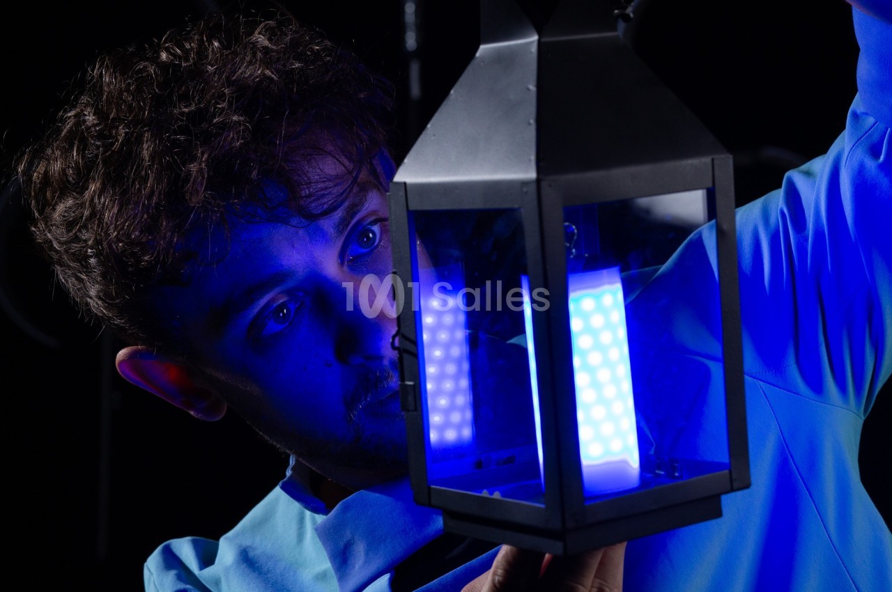 Un homme examine une lanterne émettant une lumière bleue vive dans un environnement sombre.