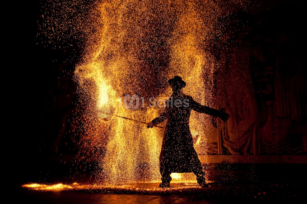 Personne en manteau et chapeau manipulant des étincelles incandescentes dans un environnement sombre.