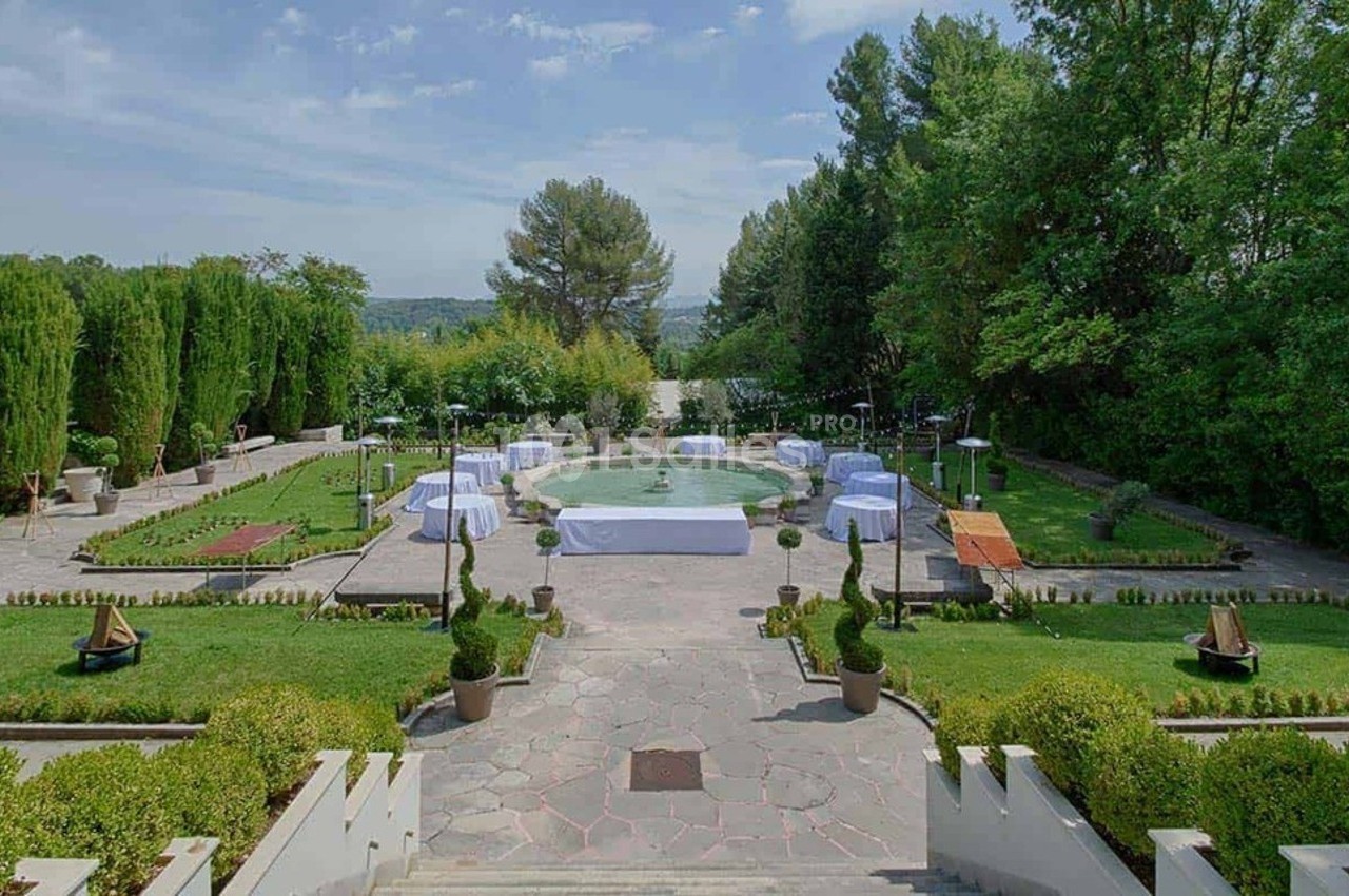 Vue d'un jardin aménagé avec une fontaine centrale, entouré de verdure et de tables décorées pour un événement.