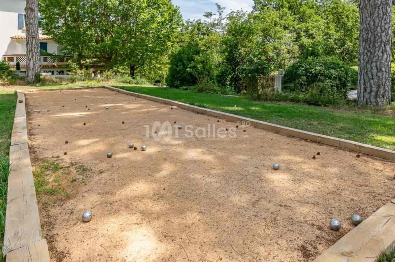 Terrain de pétanque en plein air entouré de verdure, avec des boules dispersées sur le sol sablonneux.