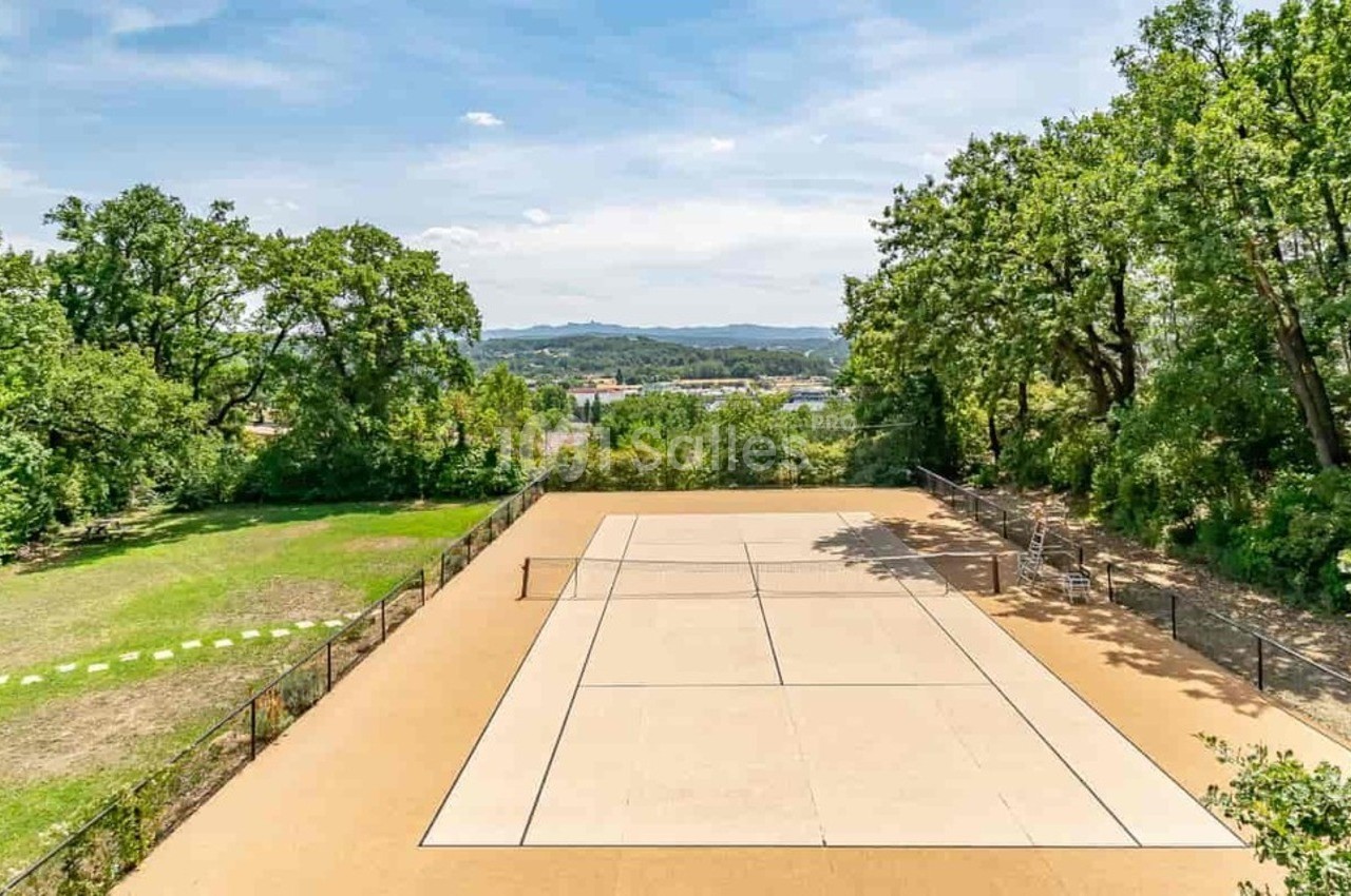 Terrain de tennis en plein air entouré d'arbres et de verdure, avec une vue dégagée sur l'horizon.