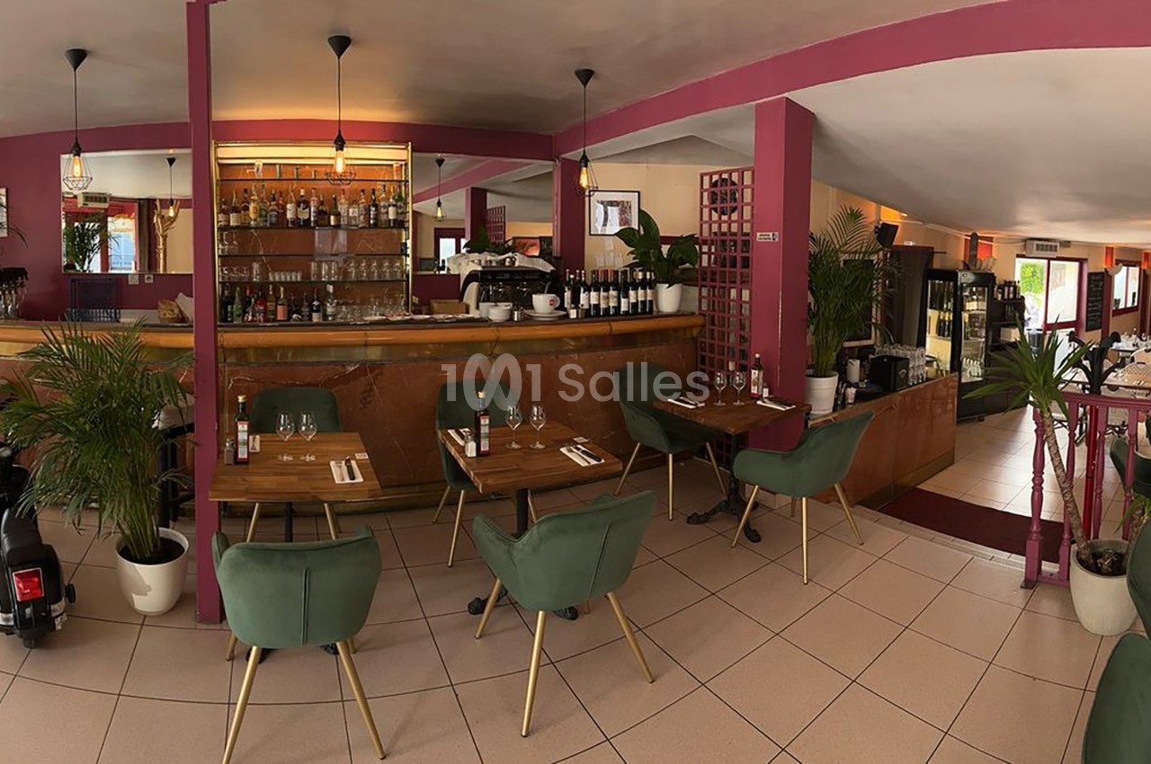 Salle de restaurant lumineuse avec tables dressées, chaises vertes, bar en bois et décoration végétale.