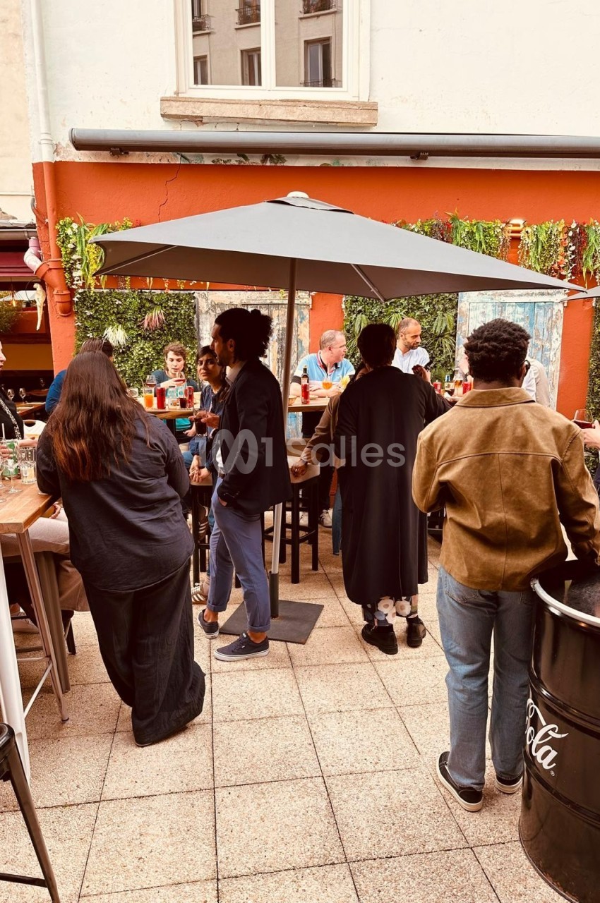 Groupe de personnes discutant et partageant un moment convivial sur une terrasse extérieure avec parasol.