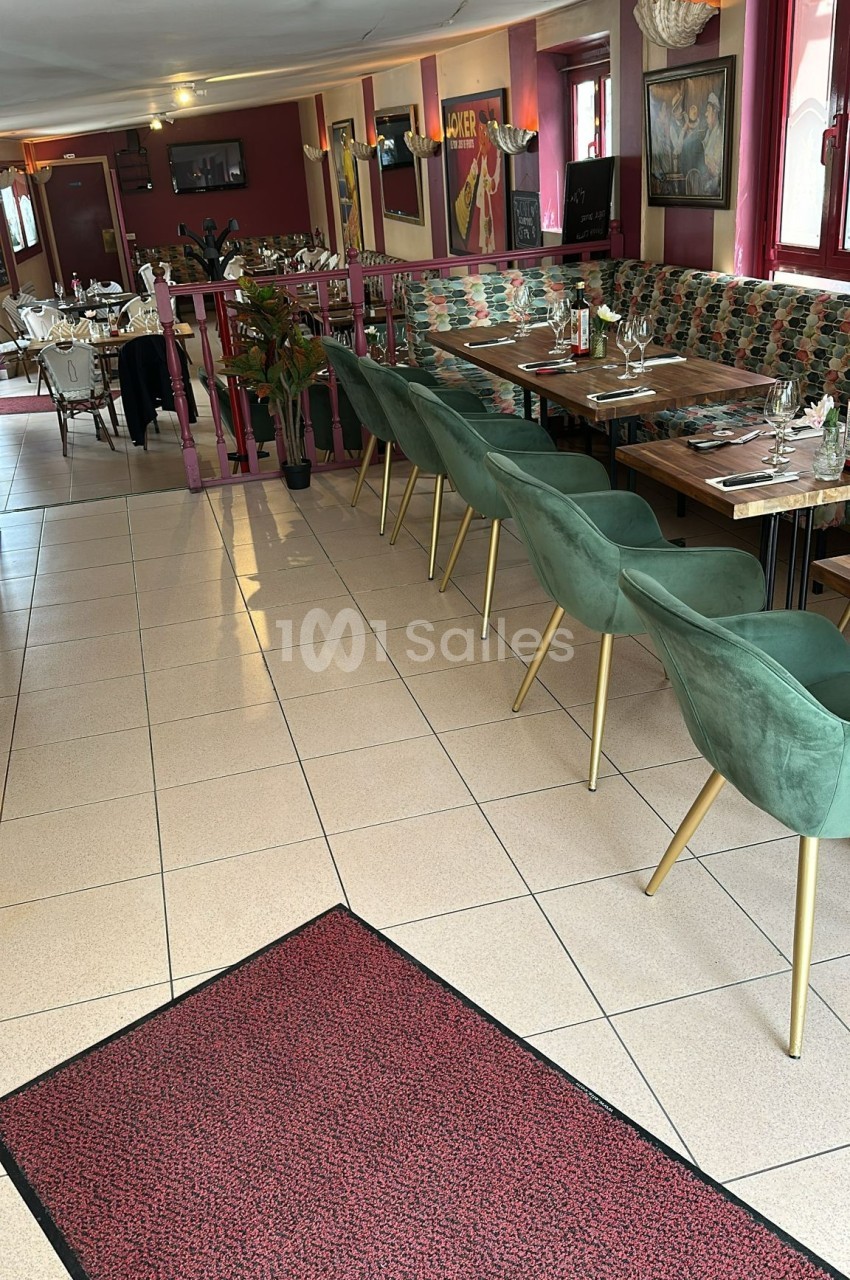 Salle de restaurant avec tables dressées, chaises vertes et décoration intérieure aux tons rouges et verts.