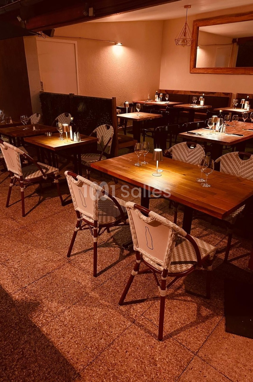 Salle de restaurant avec tables en bois, chaises en rotin et éclairage tamisé créant une ambiance chaleureuse.