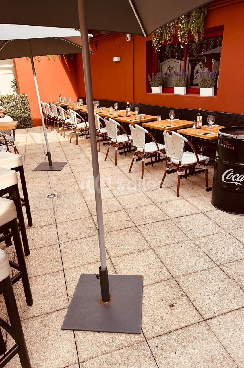 Terrasse extérieure avec tables et chaises alignées, parasols ouverts et mur rouge en arrière-plan.
