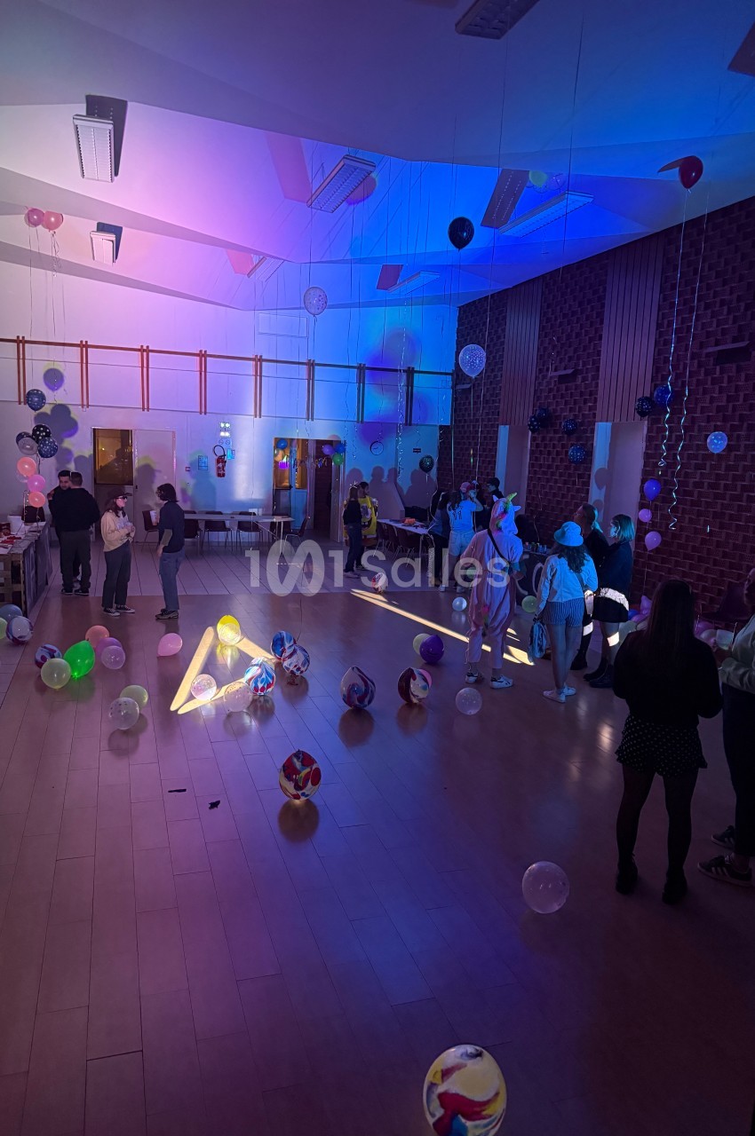 Salle décorée avec des ballons lumineux, éclairée par des lumières colorées, avec des personnes discutant et se déplaçant.