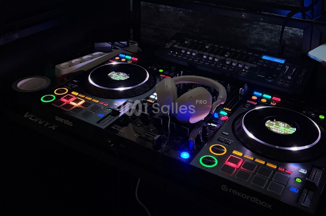 Table de mixage DJ avec platines lumineuses, casque audio posé au centre et équipement électronique en arrière-plan.