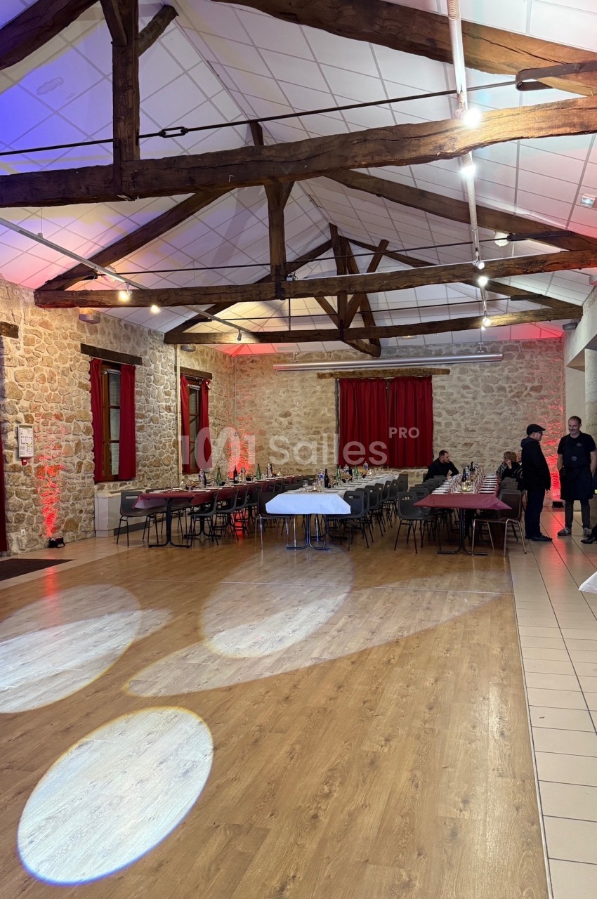 Salle de réception avec murs en pierre, poutres apparentes, tables dressées et éclairage tamisé.