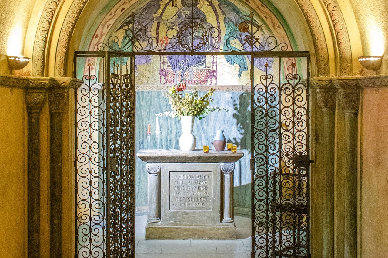 Autel décoré de fleurs dans une petite chapelle ornée de fresques et encadrée par une grille en fer forgé.