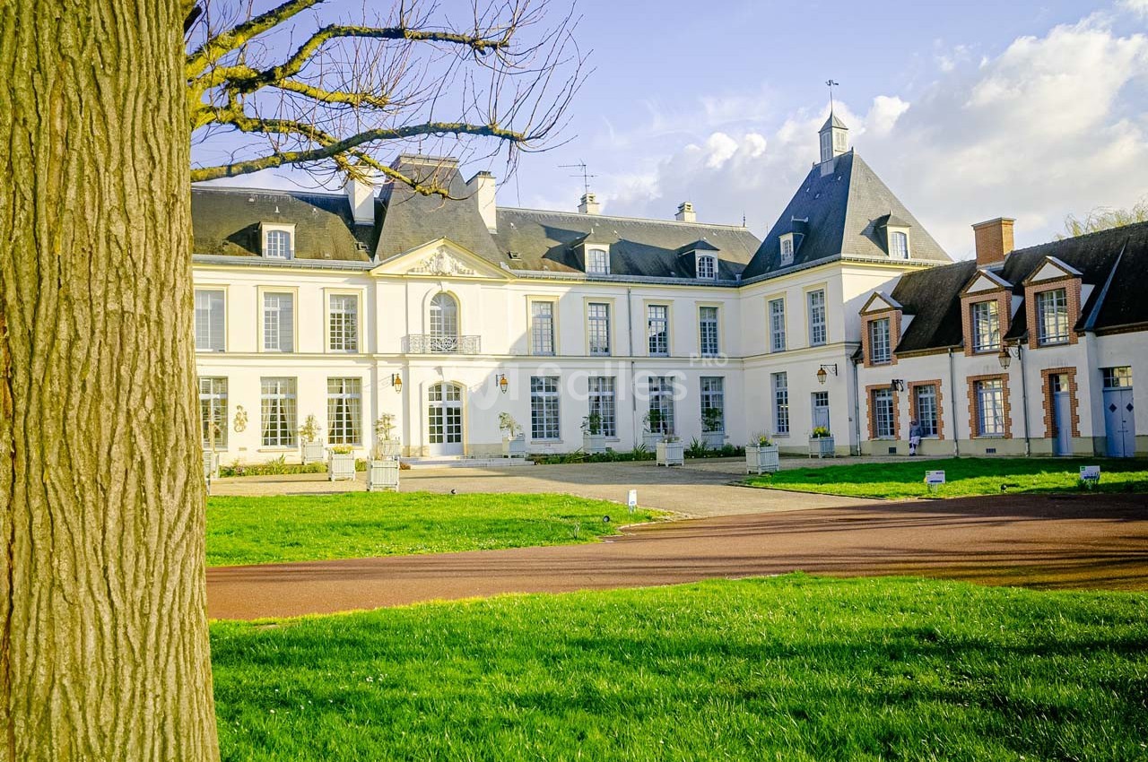 Façade d'un château blanc entouré de pelouses, avec un ciel bleu et quelques nuages en arrière-plan.