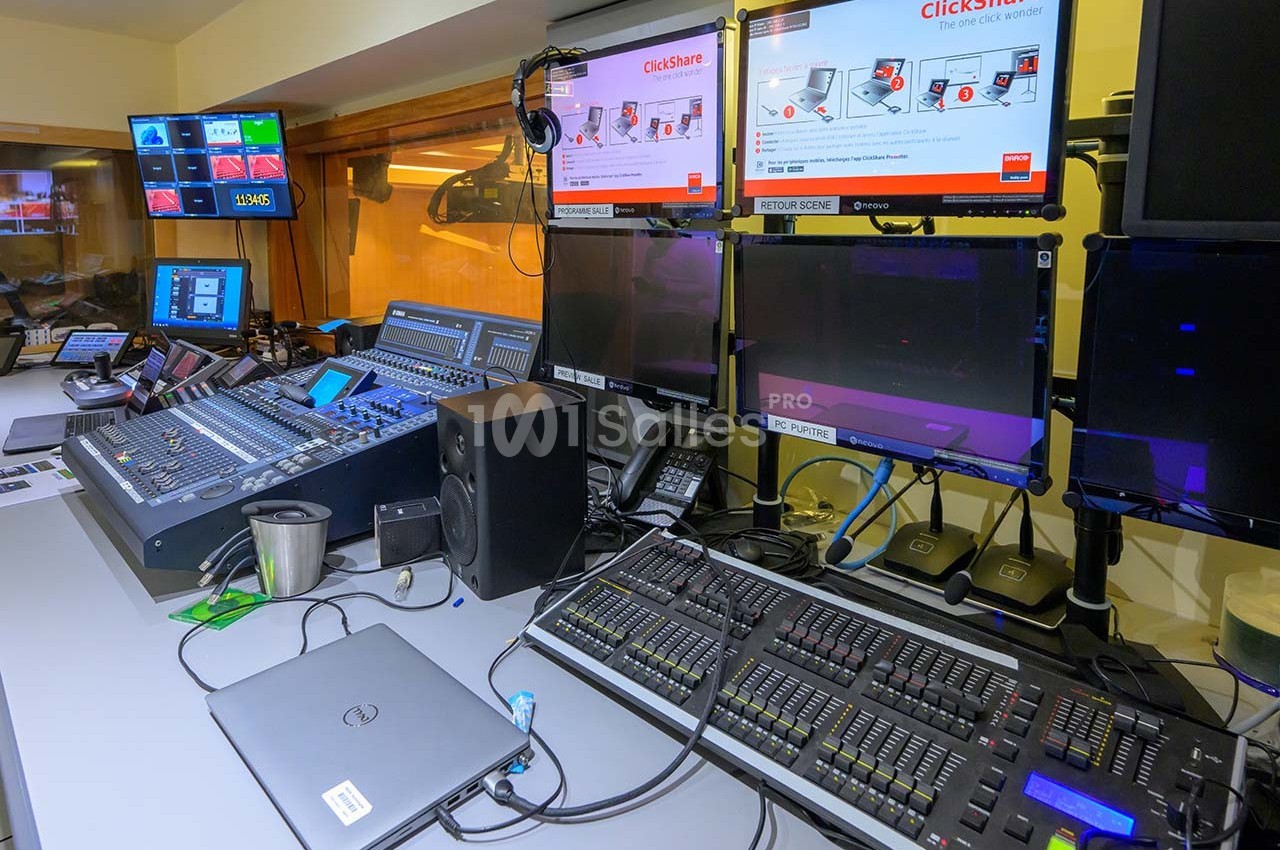 Poste de contrôle audiovisuel avec consoles de mixage, écrans, ordinateurs et équipements techniques dans une salle.