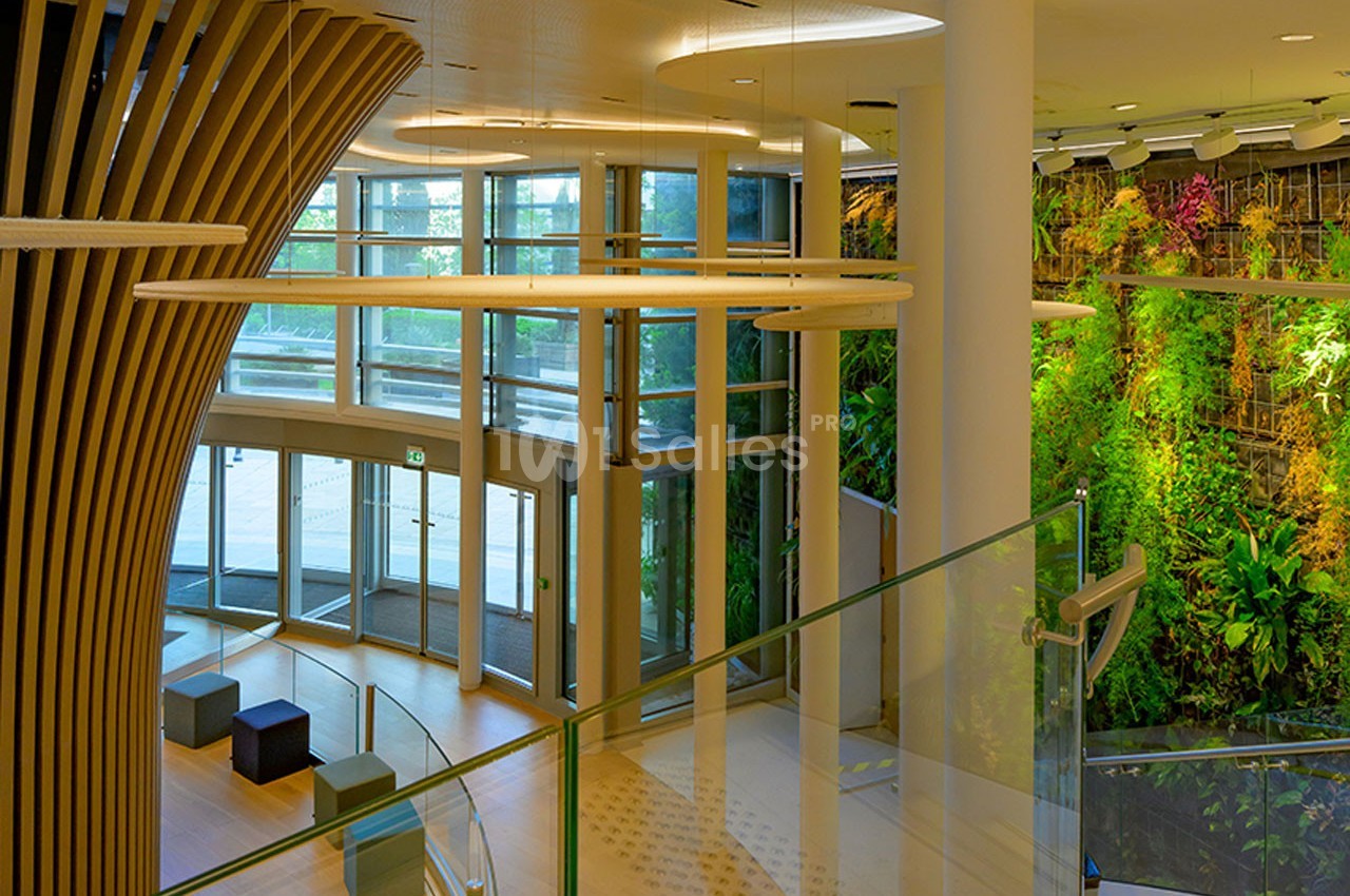 Entrée lumineuse avec des murs végétalisés, des sièges modernes et une structure en bois incurvée.