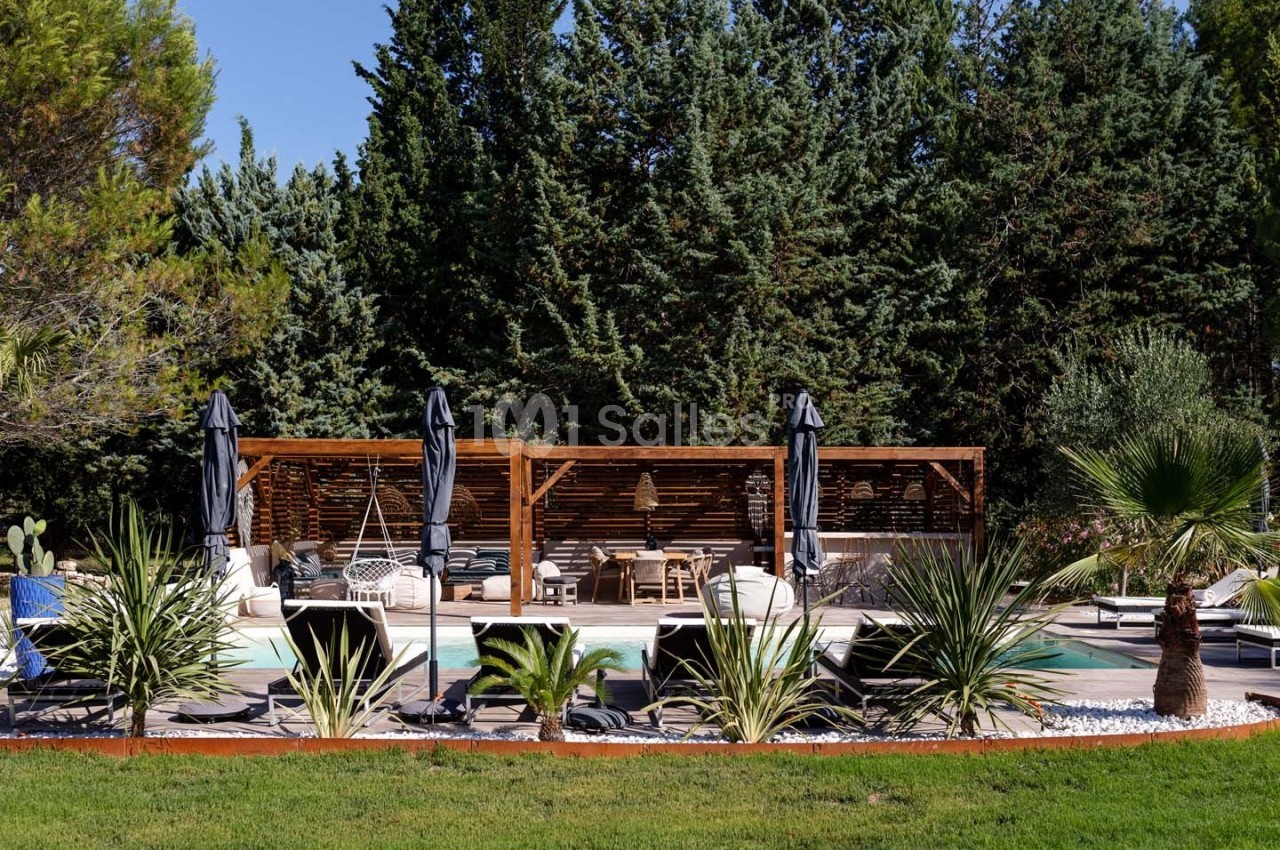 Terrasse avec piscine entourée de végétation, mobilier d'extérieur sous une pergola en bois et parasols noirs.