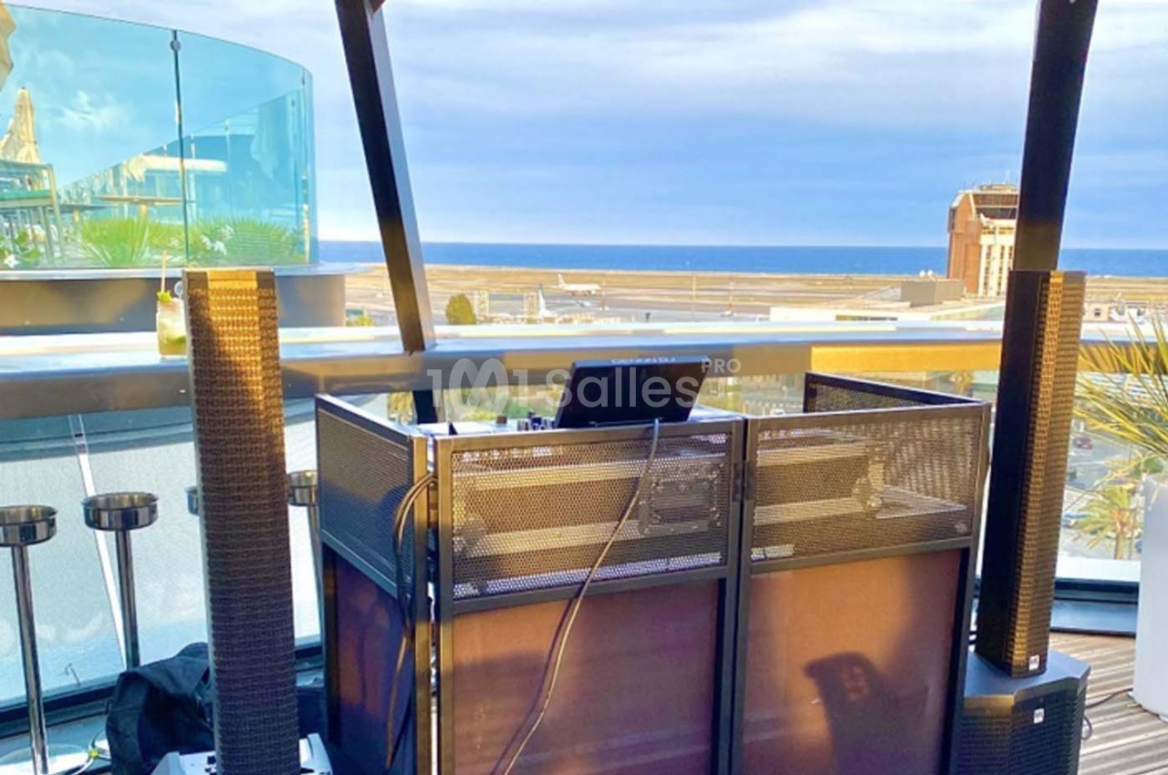 Poste de DJ installé sur une terrasse avec vue sur la mer et un ciel partiellement nuageux.