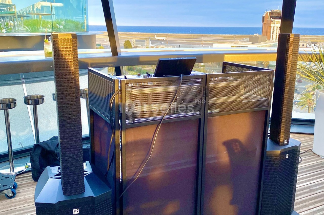 Poste de DJ avec équipement audio professionnel installé sur une terrasse offrant une vue sur la mer et des bâtiments.