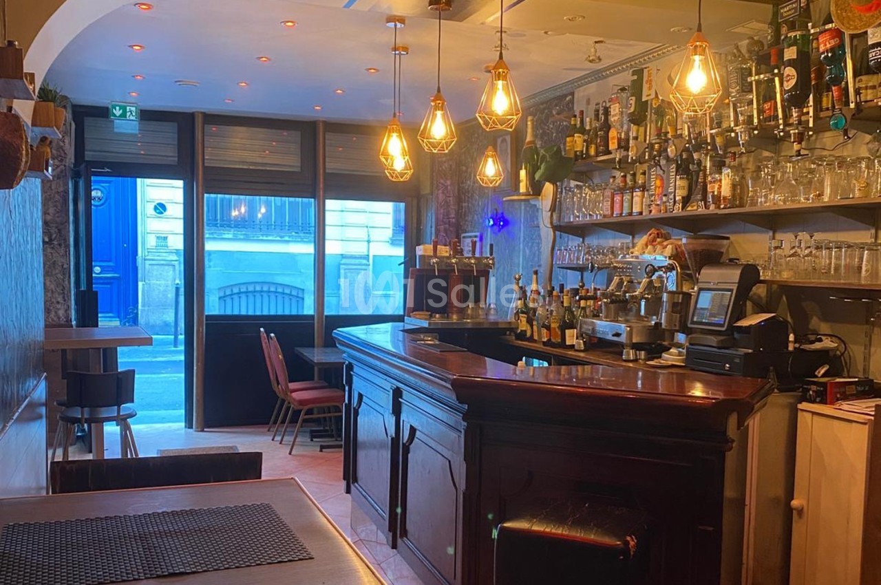 Intérieur d'un bar avec comptoir en bois, étagères remplies de bouteilles et lumière tamisée.