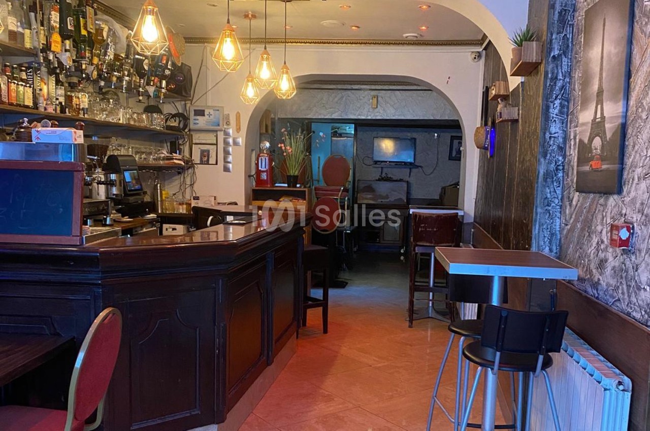 Intérieur d'un bar avec comptoir en bois, tabourets, éclairage chaleureux et décoration murale.